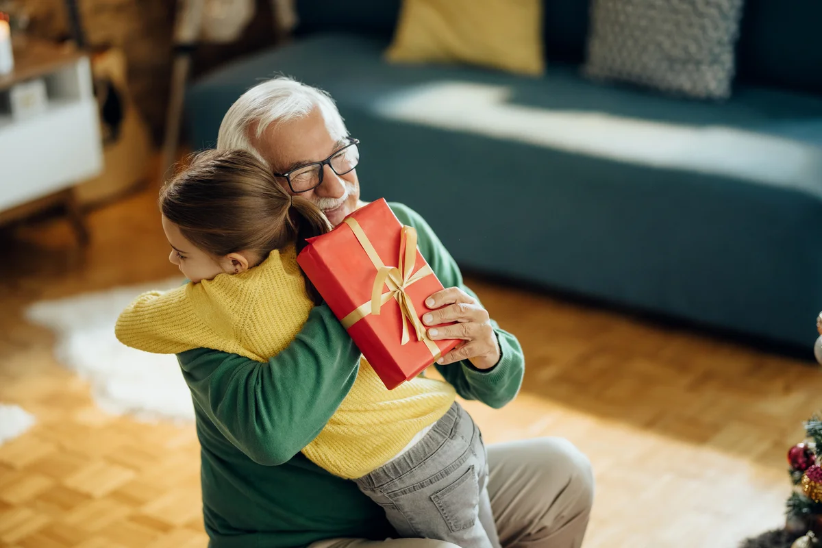 Grateful little girl embracing her grandfather while giving him a present