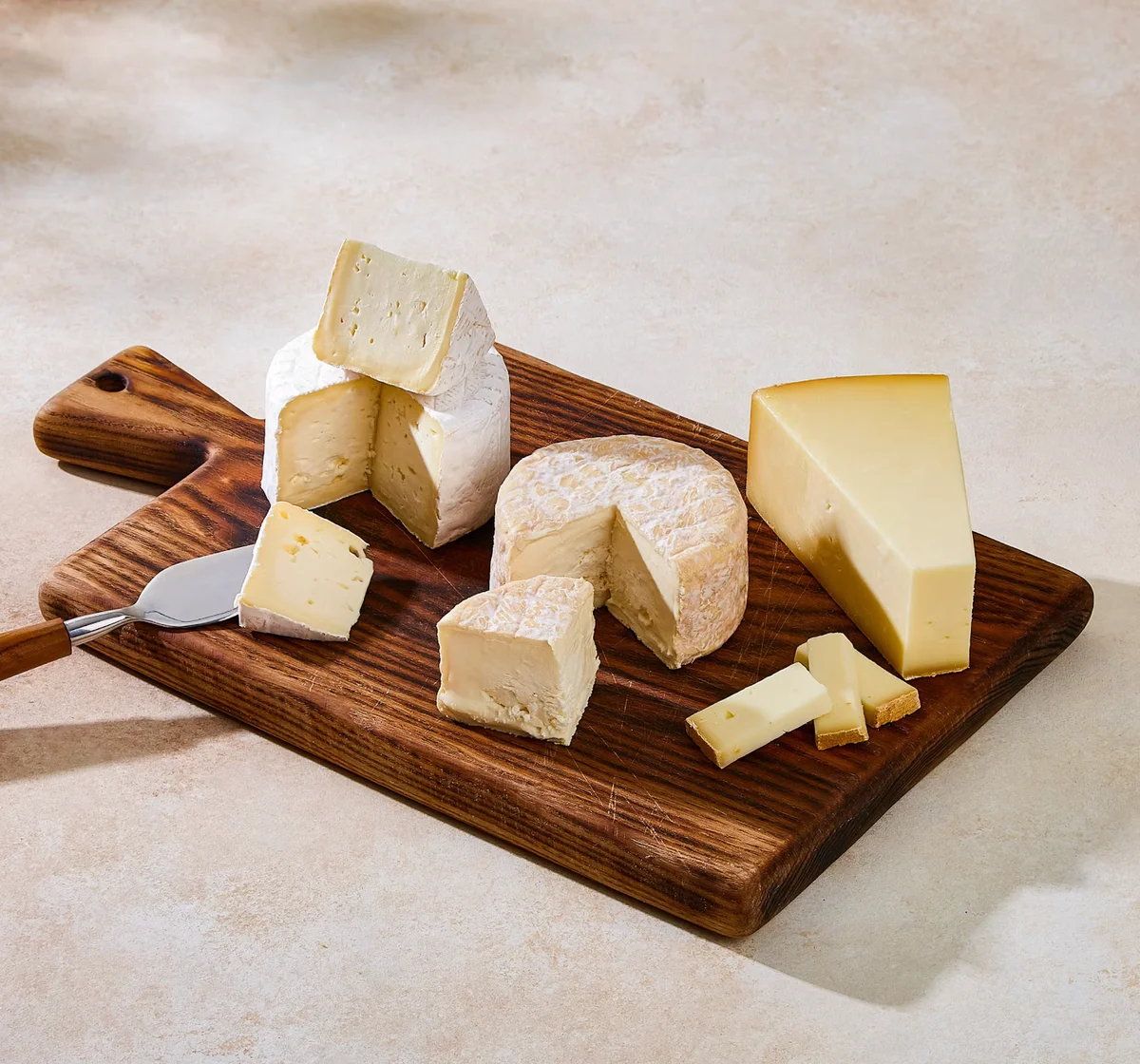 Wooden board with three gourmet cheeses.
